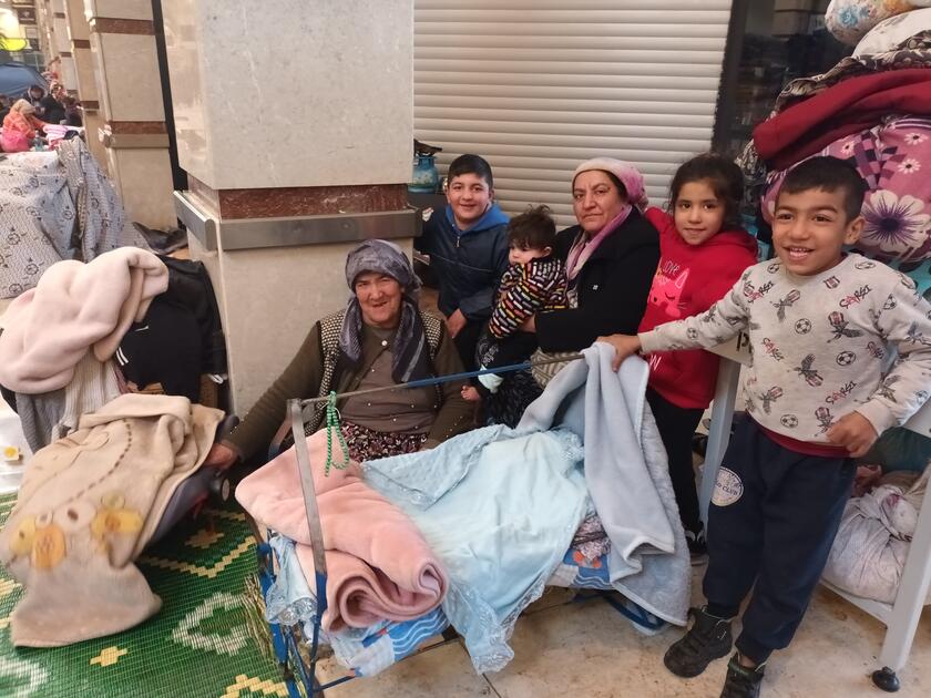 Zwei Frauen mit Kopftuch sitzen mit mehreren Kindern in einer Notunterkunft.