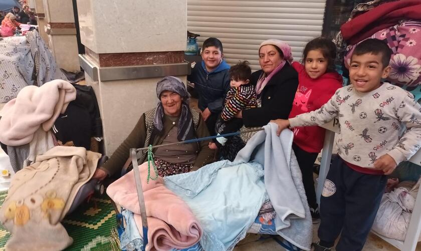 Zwei Frauen mit Kopftuch sitzen mit mehreren Kindern in einer Notunterkunft.