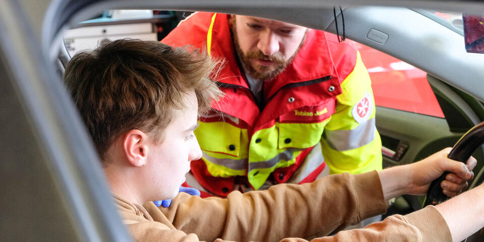 Ein Verletztendarsteller sitzt im Auto und wird von Sanitäter der Johanniter untersucht.