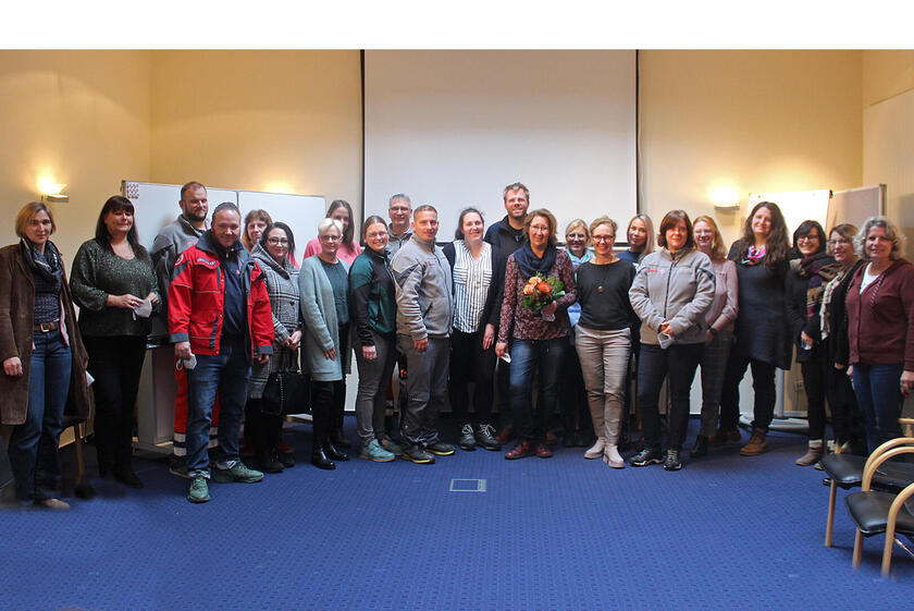 Eine Frau mit Blumenstrauß im kreise von Menschen