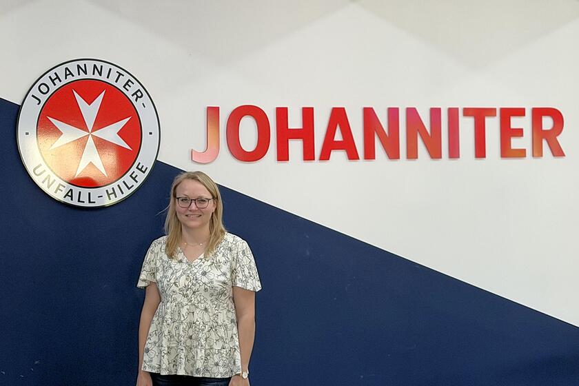 Eine blonde Frau mit Brille vor einer Wand mit Johanniter-Logo
