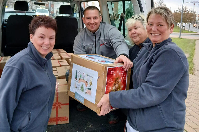 Drei Frauen überreichen einem Mann, der auf der Ladefläche eines Bullis hockt, Pakete