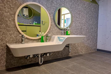 Kindgerechter Waschbereich mit niedrigen Becken, grauen Fliesen und viel Platz.