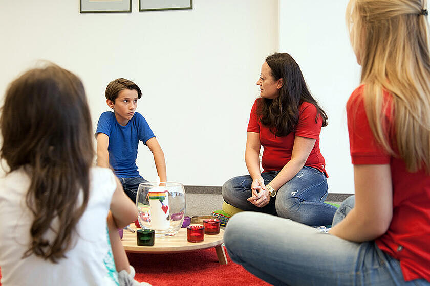 Kinder im Grundschulalter sitzen mit einer Johanniterin im Gesprächskreis beim Trauerzentrum Lacrima. In der Mitte: eine brennende Kerze.