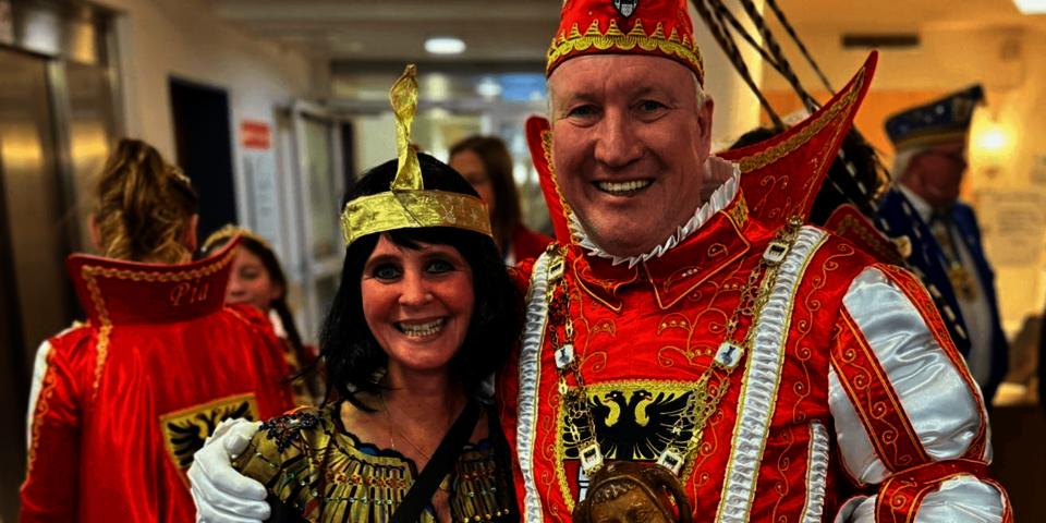 Karnevalsprinz in Uniform posiert mit verkleideter Begleiterin im Innenraum.