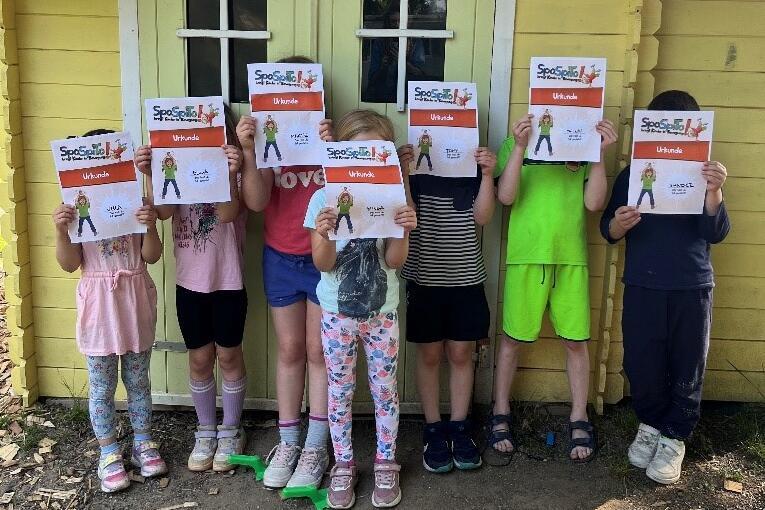 Sieben Kita-Kinder stehen mit ihren Urkunden stolz vor dem Spielehäuschen der Kita Ritternest.