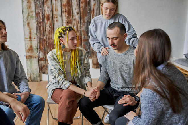 Ein Gruppe junger Menschen tröstet einen trauernden Mann.