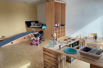 Ein Raum mit Spielküche sowie Bett und Esstisch mit Stühlen.