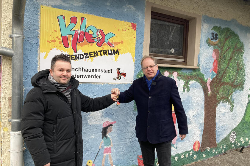 Einem Mann wird vor dem Schild des Jugendzentrums von einem anderen Mann ein Schlüssel überreicht.