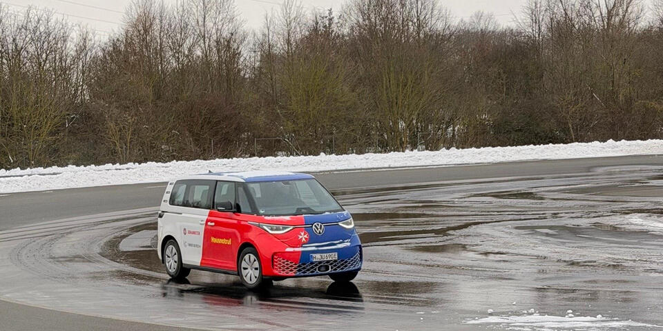 Ein VW-Bulli fährt auf nasser Fahrbahn Kurven.