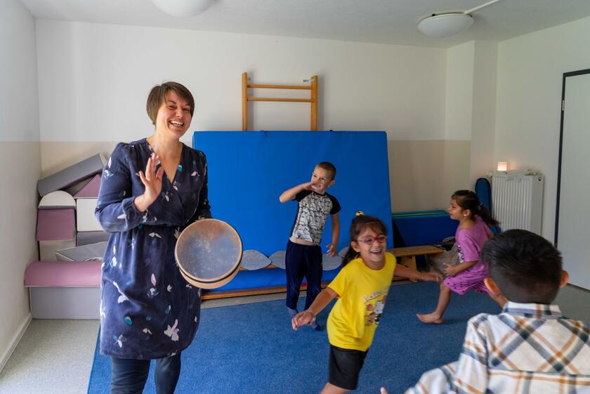 Eine Frau schlägt eine Trommel, während Kinder dazu tanzen.