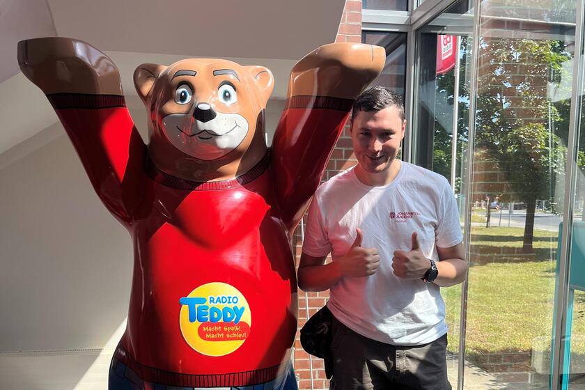 Ein Mitglied der Johanniter-Jugend posiert neben der Bärenfigur von Radio Teddy und gibt zwei Daumen hoch.