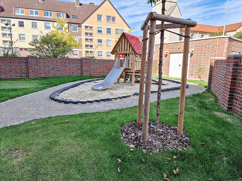 Eine Rutsche auf einem Außengelände mit Rasen. Im Hintergrund eine Kirche.