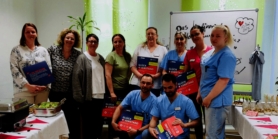 acht Frauen, einige in Pflege-Berufskleidung, stehen nebeneinander neben einem Buffet, vor ihnen hockend zwei Männer