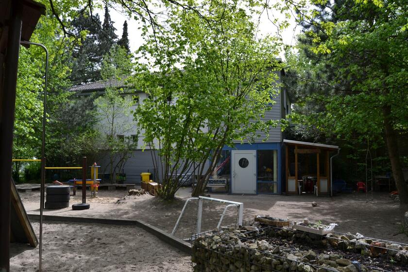 Vor dem Kitagebäude gibt es Sand, Bäume, ein kleines Fußballtor und Hochbeete mit Kräutern.