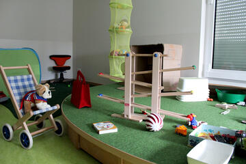 Kugelbahn, Kinderwagen und Kuscheltiere neben und auf dem Spielteppich im Gruppenraum.