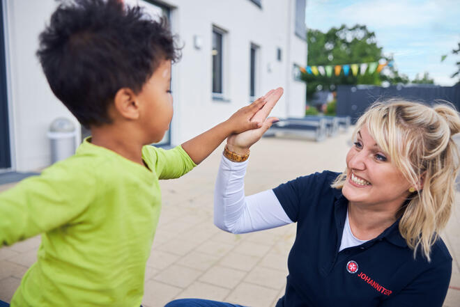 Eine Erzieherin gibt einem Kind ein "High Five" in einer Kindertagesstätte.