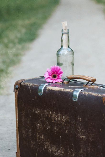 Koffer auf dem Weg mit Blume und Flaschenpost