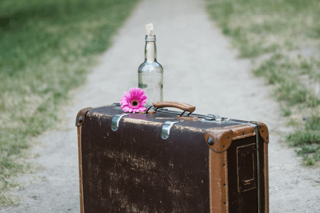 Koffer auf dem Weg mit Blume und Flaschenpost