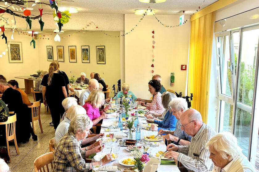 An einem lange Tisch sitzen sich essende Menschen gegenüber. 