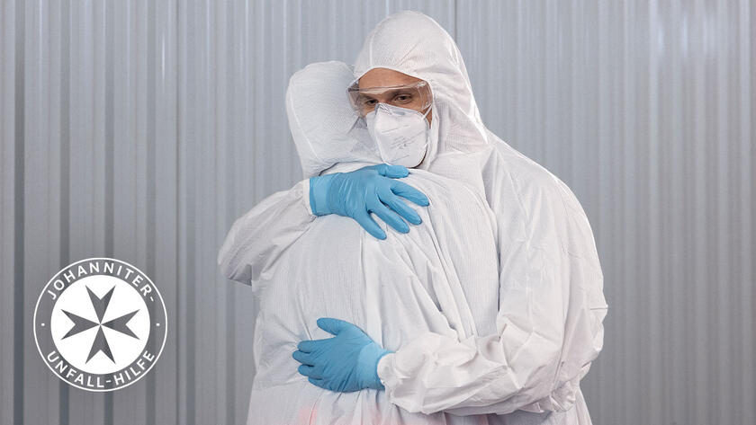 Zwei Personen in Schutzausrüstung während der Pandemie umarmen sich