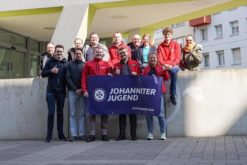 Mehrere Mitglieder der Johanniter-Jugend stehen in einer Gruppe in Braunschweig und halten eine Fahne in den Händen