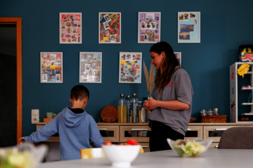 Betreuerin spricht mit einem Jungen in einem Raum mit Fotocollagen an der Wand.