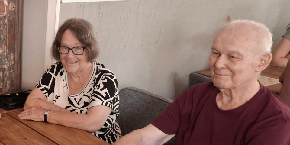 eine Frau und ein Mann sitzen an einem Tisch und lächeln in die Kamera