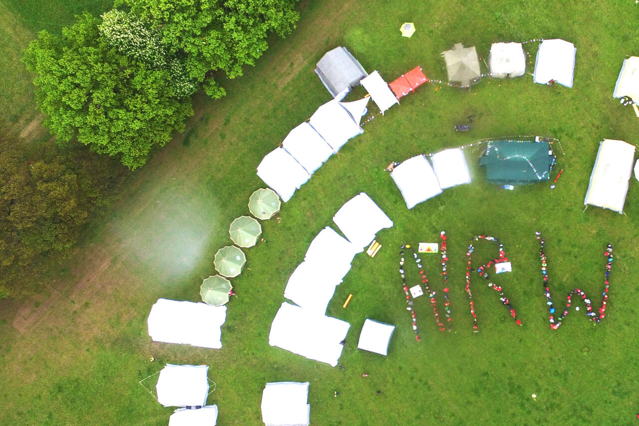 Eine Luftaufnahme von Zelten, die im Kreis angeordnet sind. In der Mitte bilden Menschen die Buchstaben N R W.