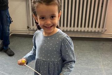 Ein kleines Mädchen im blauen Kleid mit Zöpfen lacht in die Kamera.