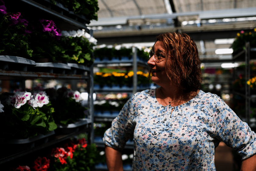 Pflegerin in einer Gärtnerei betrachtet Blumenregale, lächelnd.  