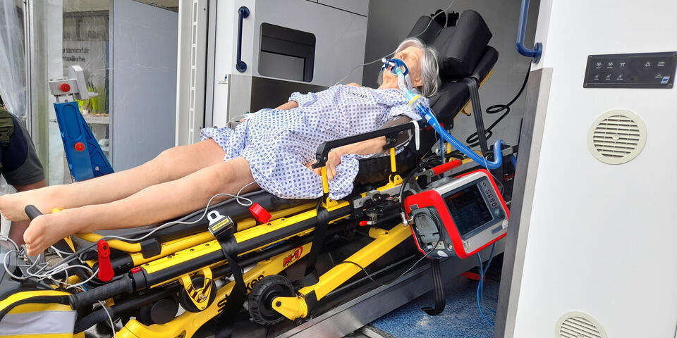 Eine Simulationspuppe wird auf einer trage in einen Rettungswagen geschoben