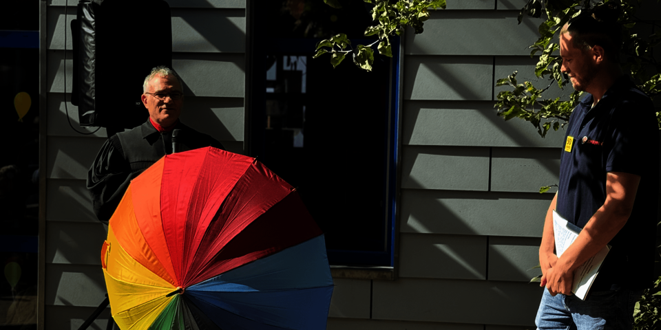 Ein Geistlicher mit Regenbogen-Regenschirm steht neben einem Mann im Johanniter-Teamshirt.