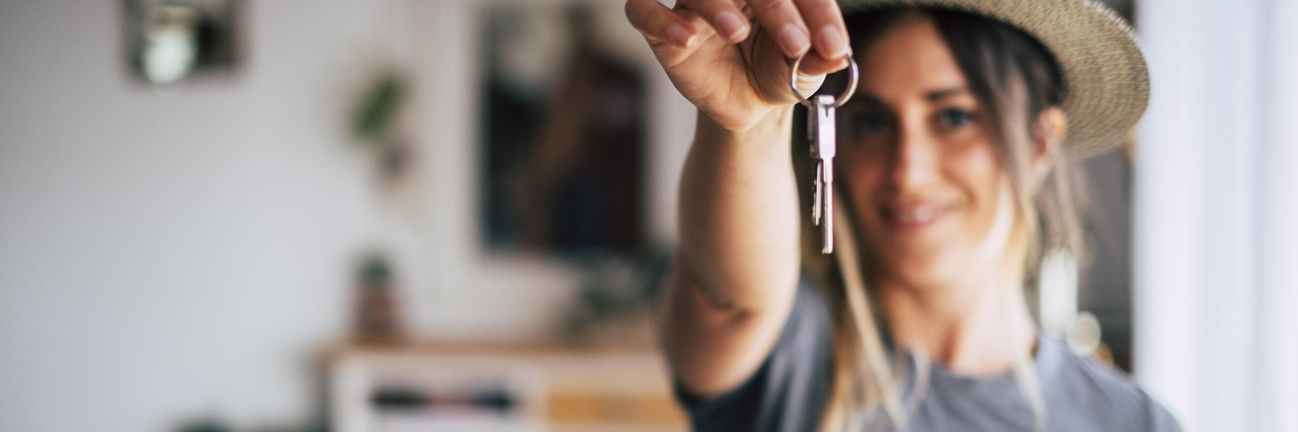 Eine Frau mit Hut hält einen Schlüsselbund in die Höhe