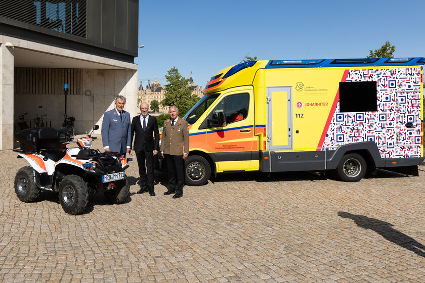 Auf dem Bild sind drei Personen zu sehen (Georg Khevenhüller, Christian Pegel, Volker Bescht) stehend neben zwei Einsatzfahrzeugen