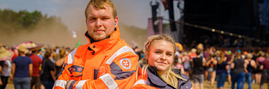 Zwei Mitarbeitende im Sanitätsdienst lehnen Rücken an Rücken auf einem Festivalgelände.