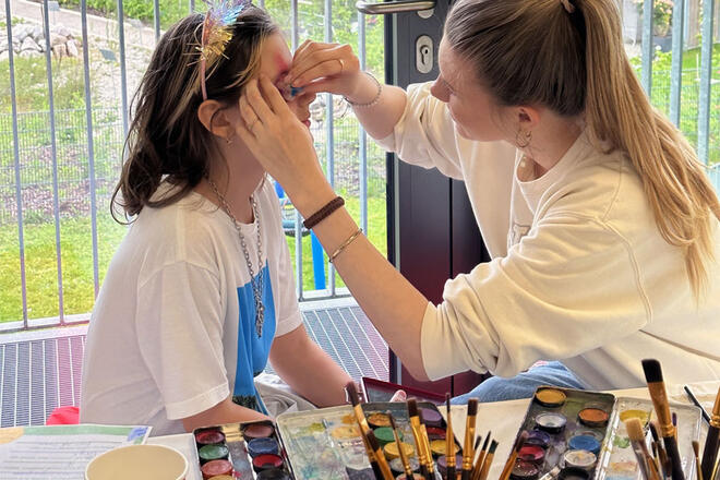 Eine Frau schminkt ein Kind mit Gesichts-Malfarben.