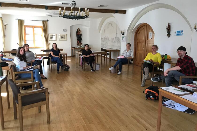 Mehrere Leute sitzen in einem Stuhlkreis in einem großen Raum.