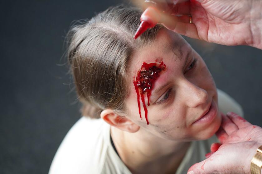 Einer Mime wird für eine Übung eine blutende Kopfwunde geschminkt