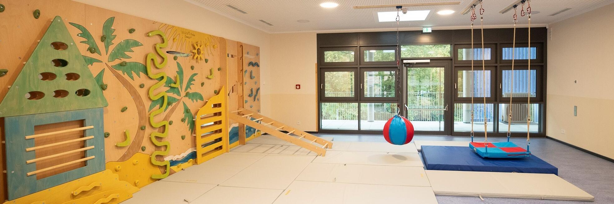 Ein Turnraum mit Matten, Kletterwand, Bällen und Schaukeln.