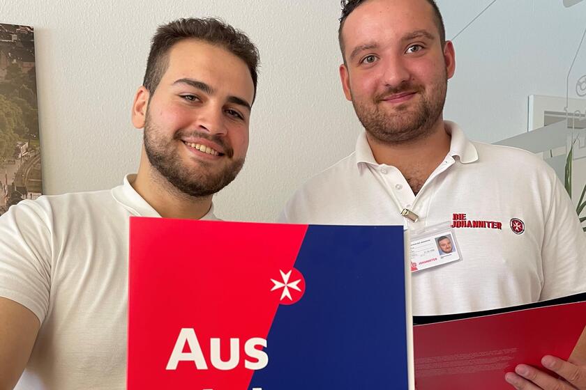 Zwei Mitarbeiter halten eine Johanniter-Broschüre in die Kamera