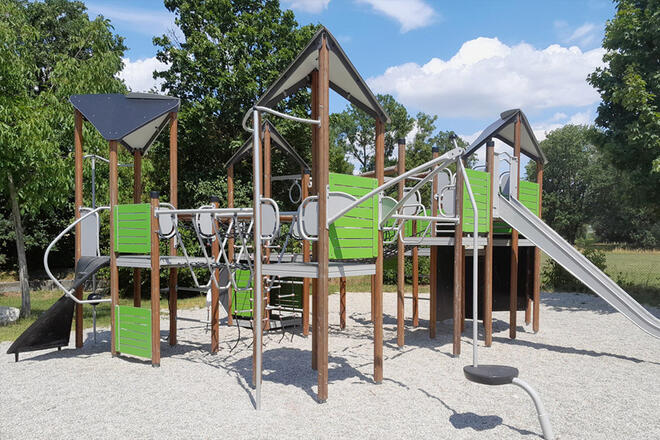 Ein Spielplatz mit mehreren Klettergerüsten und Rutsche auf einer Kiesfläche.
