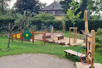 Sandkasten und weitere Außenspielgeräte umgeben von Grünflächen.