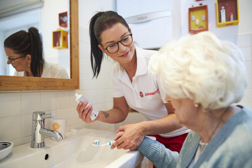 Eine Mitarbeiterin der Johanniter hilft einer älteren Dame beim Zähneputzen.