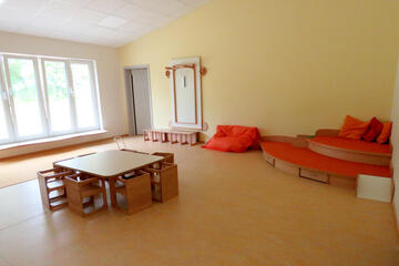 Spielecke im Gruppenraum mit gemütlichen orangefarbenen Kissen und zahlreichen Spielsachen.