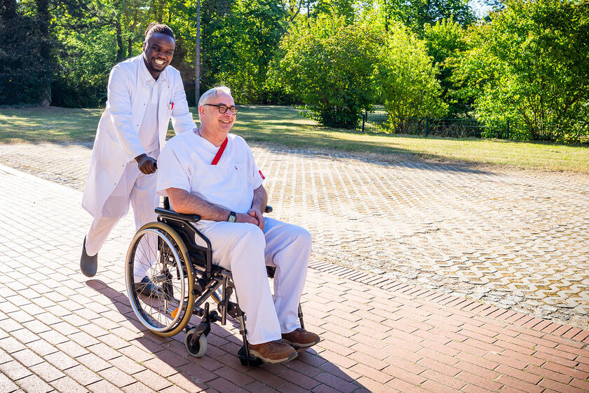 Mann im Rollstuhl wird von einem Arzt geschoben