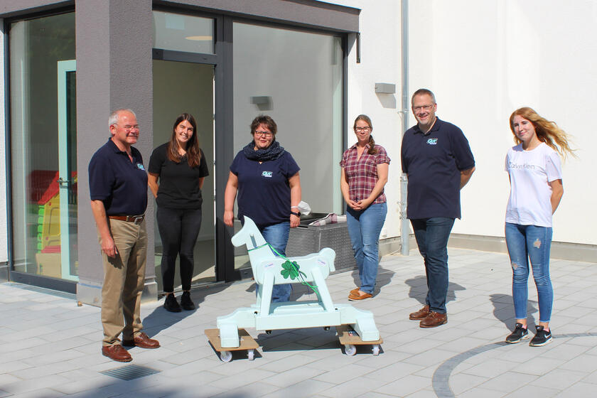 zwei Männer und vier Frauen hinter einem Holzschaukelpferd