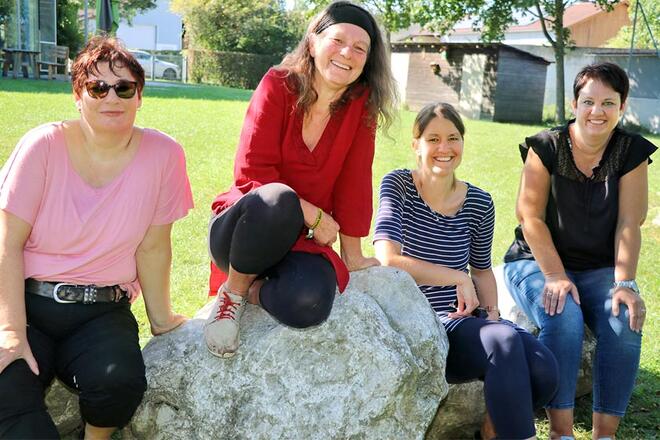 4 Frauen sitzen auf Steinen auf einer großen Grünfläche und lächeln in die Kamera.