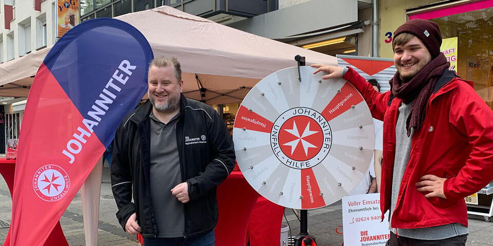 Zwei Mitarbeiter stehen am Glücksrad auf dem Schängelmarkt 2022