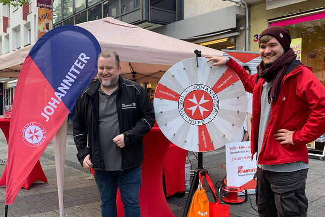 Zwei Mitarbeiter stehen am Glücksrad auf dem Schängelmarkt 2022